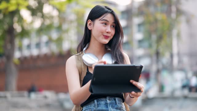 Asian female traveler using a tablet for notes or drawings and relaxing at a tourist spot in a northern province of Thailand