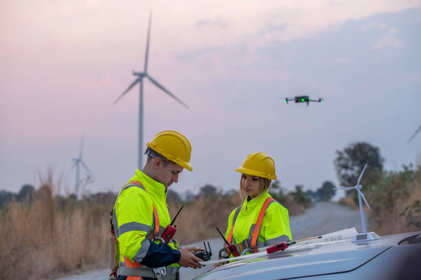 istock Engineer wearing uniform read blueprint document inspection work in wind turbine farms rotation to electricity,standing in front of car Model windmill and wind force meter is ecology energy concept. 2047117248