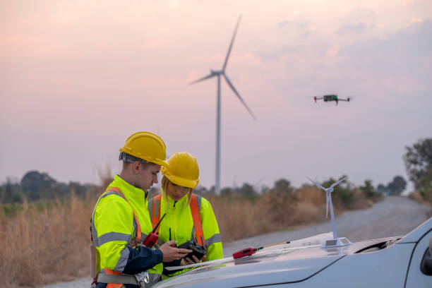 istock Engineer wearing uniform read blueprint document inspection work in wind turbine farms rotation to electricity,standing in front of car Model windmill and wind force meter is ecology energy concept. 2047117759