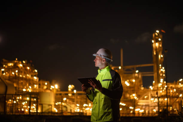 istock Engineer survey team wear uniform and helmet stand workplace checking blueprint project and radio communication inspection work construction site with night lights oil refinery background. 2047155905