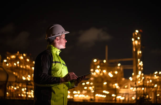 istock Engineer survey team wear uniform and helmet stand workplace checking blueprint project and radio communication inspection work construction site with night lights oil refinery background. 2047155927