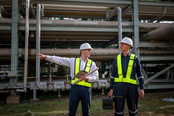 istock Engineer survey team wear uniform and helmet stand workplace checking blueprint project , radio communication and engineer box inspection work construction site with pipe oil refinery background. 2047157254