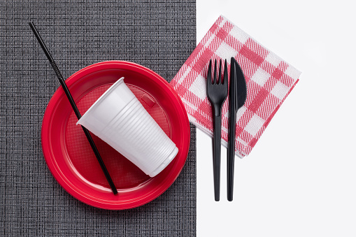Plastic colored utensils on a black table, white background. Plastic recycling.