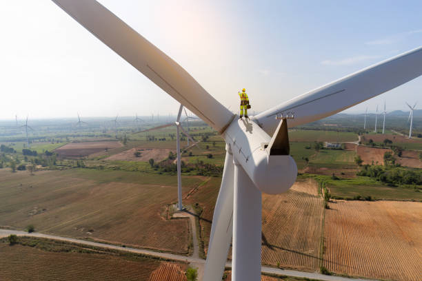 istock Engineer wearing uniform holding equipment box standing[ on windmill under work inspection and checking survey. Windmill turbine farm rotation to electricity energy. 2047172460