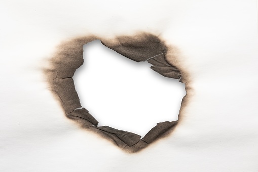 A charred, irregular hole through white paper, revealing a stark white backdrop.