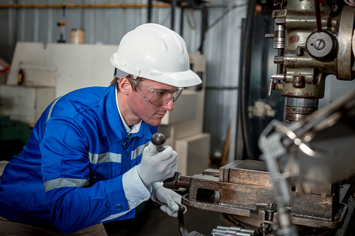 Industry engineer wearing safety uniform control operating lathe grinding machine working with detail tablet computer on hand in industry factory is metal manufacture industry concept.