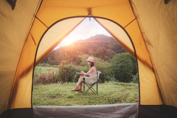 istock Happy woman freelancer traveller working online using laptop and drink a cup coffee or tea enjoying listen music stay in camping tent landscape with mountain is holiday relaxed lifestyle concept. 2047265976