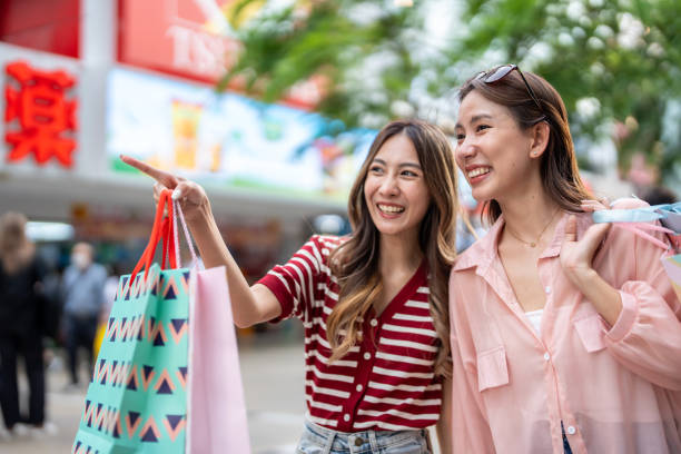 asian young women shopping goods outdoor in shopping street at night. attractive young female friends holding shopping bags then walking with happiness enjoy purchasing in department store together. - two party system ストックフォトと画像
