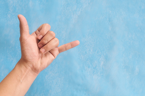Young male Asian hand making shaka sign or call me sign isolated on blue background.