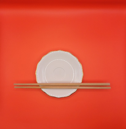 A pair of chopsticks on a plate with red background.