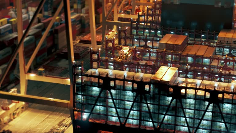 AERIAL Drone Shot of Crane Loading Container into Caro Ship Moored at Industrial Port at Night