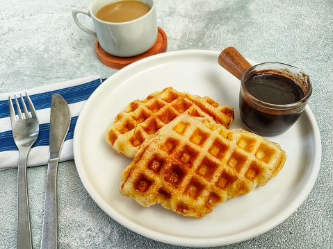 croissant waffle or croffle with dark chocolate sauce served on a white plate accompanied by a cup of hot coffee. close up, selective focus