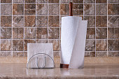 Paper napkins in chrome holder and towels on wooden holder on the table against the background of a tiled wall.
