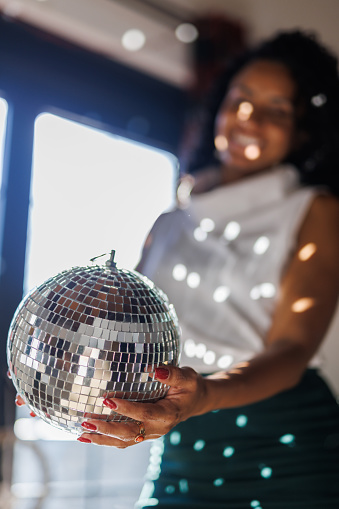 Low angle view of charming woman standing by the window, holding a disco ball that is making an interesting light pattern on her.