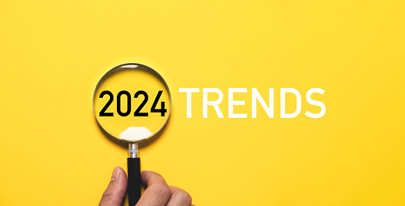 Hand holding magnifier glass with 2024 trends for marketing monitor and business focus planing in new year concept.