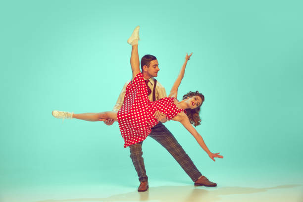 Swing dancers radiating happiness while performing energetic dance moves in motion against gradient mint background. Concept of music, hobby, art, energy, happiness, mood, action, 60s, 70s culture