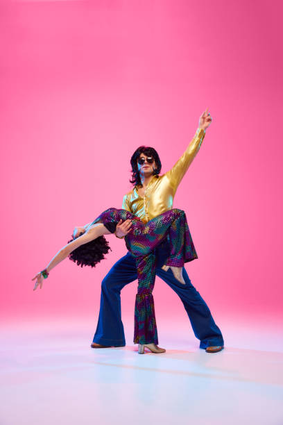 istock Disco duo mid-dance, man in bell-bottoms lifting partner against gradient pink studio background. Artists in motion. 2047443746