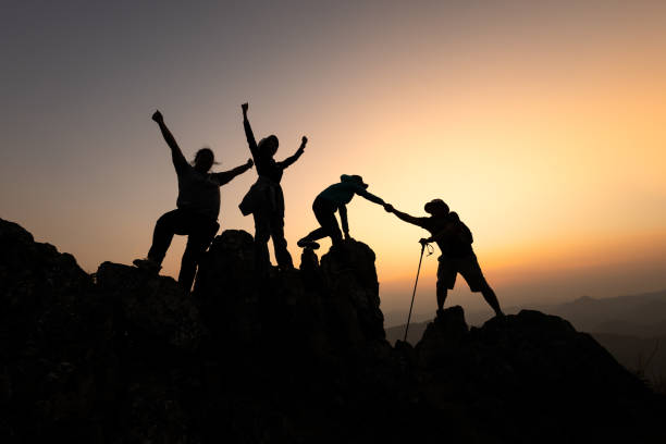 istock Silhouette of Group team tourists lends helping hand climb cliffs mountains helping hand. teamwork people climbers climb top overcoming hardships, teamwork helping hand business travel  concept. 2047444821