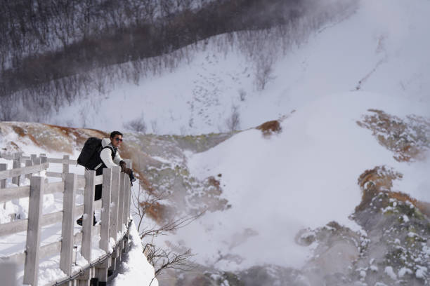 tourist walk along bridge and walk way to see great view snow ,mountain ,steam and sky at jigokudani hell valley noboribetsu Hokkaido Japan