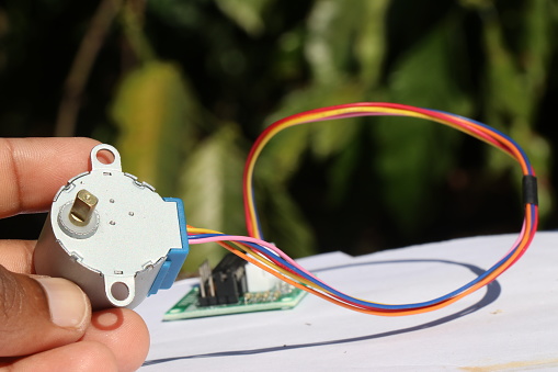 Stepper motor held in the hand that is used in many prototyping projects connected to a motor driver on the background