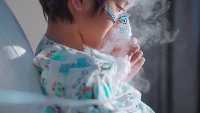 Patient boy holding and breathing with an inhaler face mask at hospital side view SLOW MO