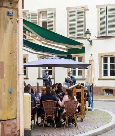 Strasbourg, France - May 19, 2021: Side view of young people eating drinking at the terrace of French restaurant on pedestrian district as bars and restaurants reopen after two months of nationwide coronavirus outbreak