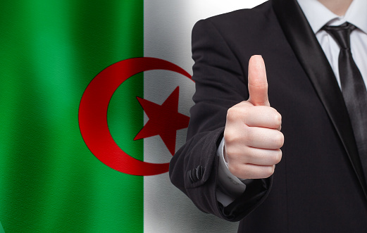 Algerian  concept. Businessman showing thumb up on the background of flag of Algeria