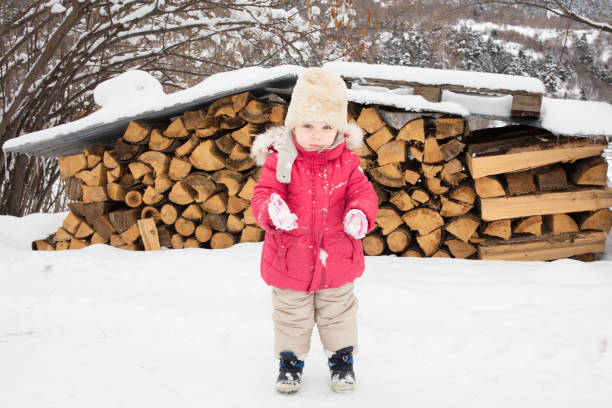A little girl wrapped in winter clothes goes to the woodshed to bring lumber for the stove. It has snowed, the short journey is magical.