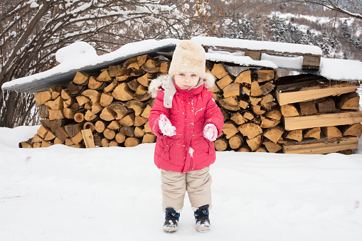 A little girl wrapped in winter clothes goes to the woodshed to bring lumber for the stove. It has snowed, the short journey is magical.