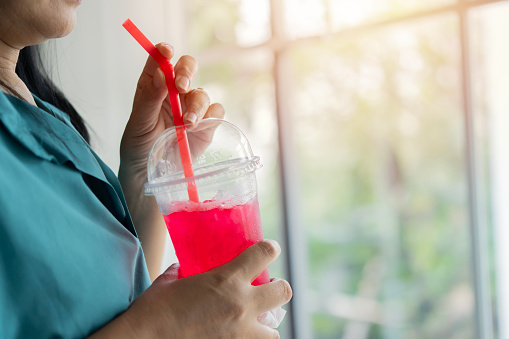 Closeup side view of woman drinking ice red soft drink by straw in the glass. Food and beverage concept.