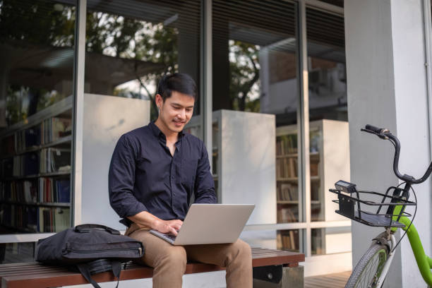 istock A young Asian businessman rides a bicycle to work. Sitting outside the office working using a laptop. 2047516640
