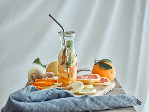 Glass of refreshing beverage made of different citrus fruits and sliced lemon orange and grapefruit on wooden board