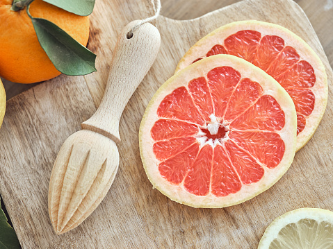 High angle of sliced fresh citrus and reamer placed on wooden chopping board near uncut delicious orange on table