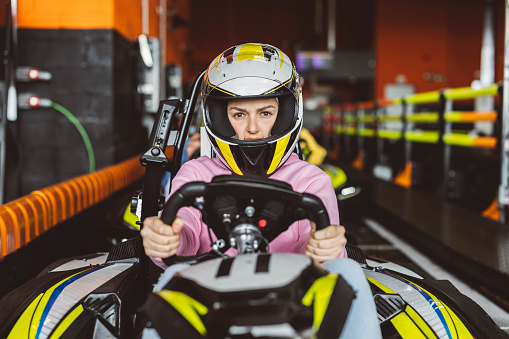 female driver looking at camera defiantly with her racing helmet holding the steering wheel of the karting car at the starting line on the circuit