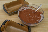 A bowl with raw chocolate dough next to prepared baking tins lined with waxed baking paper