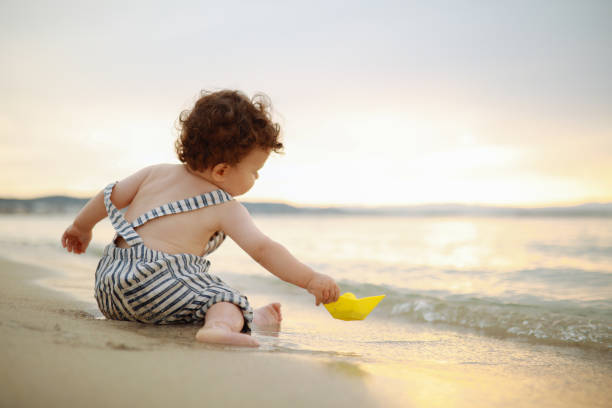 The cute baby boy playing on the beach. Little boy sitting on the sand. Sea and seashore as background with copy space