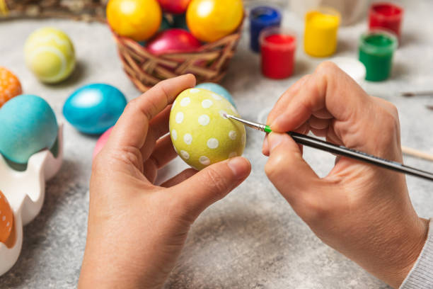 istock Woman paints Easter eggs at the kitchen wooden table.Happy Easter celebration concept.Colorful Easter eggs with different patterns.Paints,decorations for coloring eggs for holiday.Creative background. 2047581292
