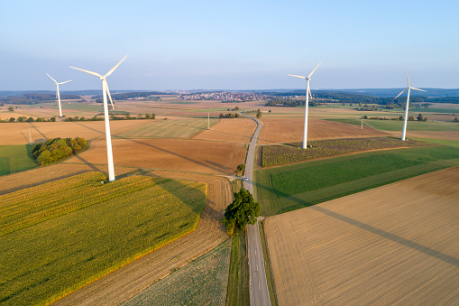 Aerial view of wind turbines among green and brown agricultural fields at sunset.
