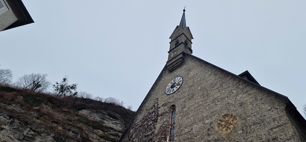 a church right next to a large hill at the church is also a clock