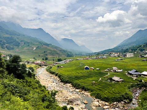 View of a valley and mountains, showing the curved terraced rice paddy fields in Sa Pa . The homesteads and farms are scattered over the area of lush green fields. A river forms a strong curved diagonal through the image.