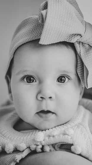 Portrait of adorable baby girl with bow in hair isolated in white background. Cute Baby, 6 months old closeup. Beautiful little girl with big eyes and bow headband on her head. Black and white photo