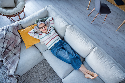 High angle view full size photo of peaceful positive lady lying comfy couch enjoy free time modern apartment inside.