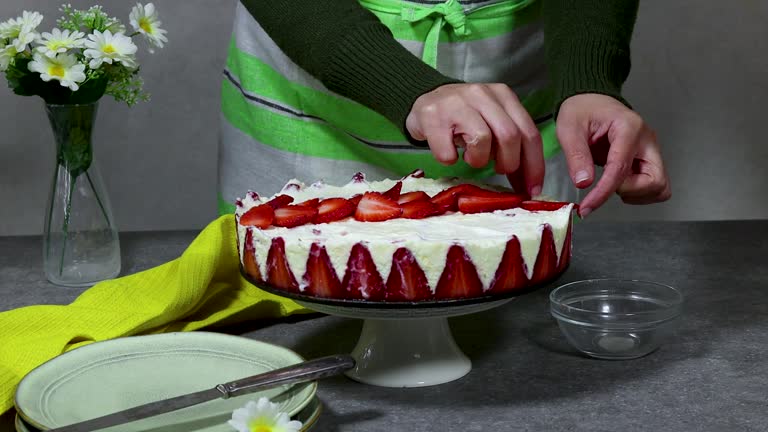 woman decorating a strawberry cake or Fraisier in french language and putting strawberry pieces