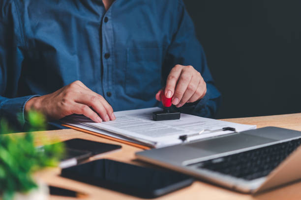 istock A person's hands are seen stamping a document, symbolizing the approval process in a professional setting. The laptop in the background suggests a modern office environment. 2047728379
