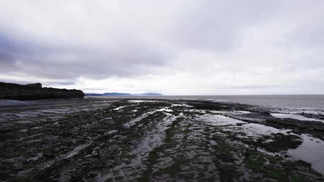 Kilve Beach in Somerset, UK is captured by a drone on a cloudy day during low tide.