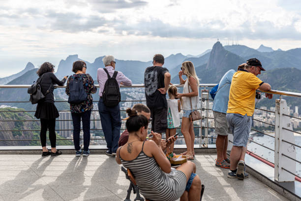 Rio de Janeiro, Brazil - December 23, 2019: The image depicts a bustling scene atop Sugarloaf Mountain's terrace, with numerous visitors engaged in sightseeing and enjoying the breathtaking views. Against the backdrop of Rio de Janeiro's skyline and natural beauty, tourists immerse themselves in the experience, capturing memories and marveling at the scenic splendor spread before them.