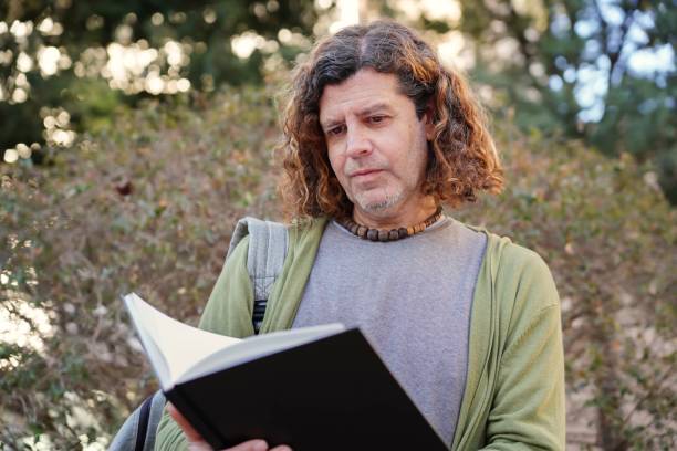 istock university professor with backpack working outside reading a notebook. world book day 2047755284