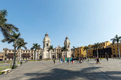 Lima, Peru - December 28, 2019: It is the vibrant heart of Peru's capital city, steeped in history and cultural significance. Surrounded by majestic colonial buildings, including the Government Palace and the Cathedral of Lima, this bustling square serves as a focal point for civic and social gatherings.\n\nThis picture portrays travelers leisurely strolling around the plaza, capturing photos, relaxing, and engaging in conversation with one another.