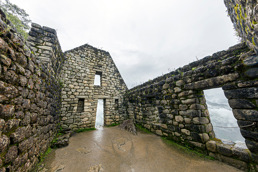 Cusco, Peru - January 3, 2020: While climbing Huayna Picchu, the picture shows the ruins of a small stone hut without a roof. Standing inside the hut, one can see dense clouds all around.