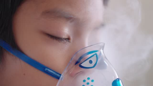 Sick Asian boy sleep while wearing an inhaler face mask side view close up handheld